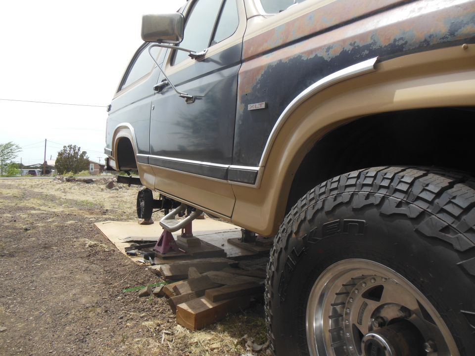 1984 Ford Bronco, side view, lifted on jack stands, showing rust and off-road tire.