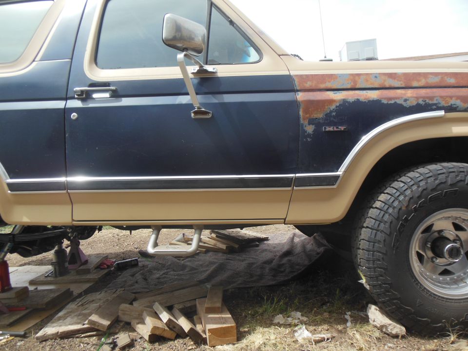 Side view of a dark blue and tan Ford Bronco with rust on the fender and a step bar.