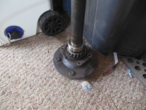 1984 Ford Bronco - A close-up view of a vehicle's axle hub and bearing assembly, resting on a carpeted floor next to a white plastic container with a black wh…