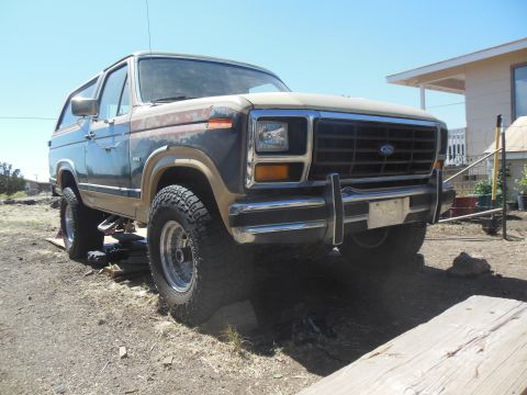1984 Ford Bronco - A lifted 1984 Ford Bronco is parked outdoors on a dirt lot under a clear blue sky. The vehicle has a two-tone paint scheme with significant…