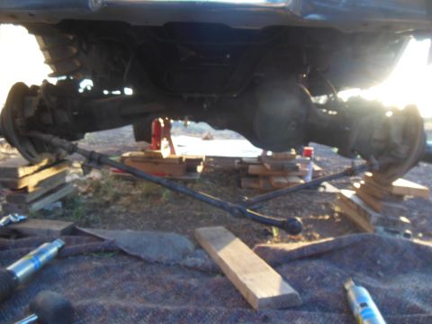 1984 Ford Bronco - The underside of a vehicle, likely a 1984 Ford Bronco, is shown with the rear axle assembly supported by wooden blocks and jacks. The steer…