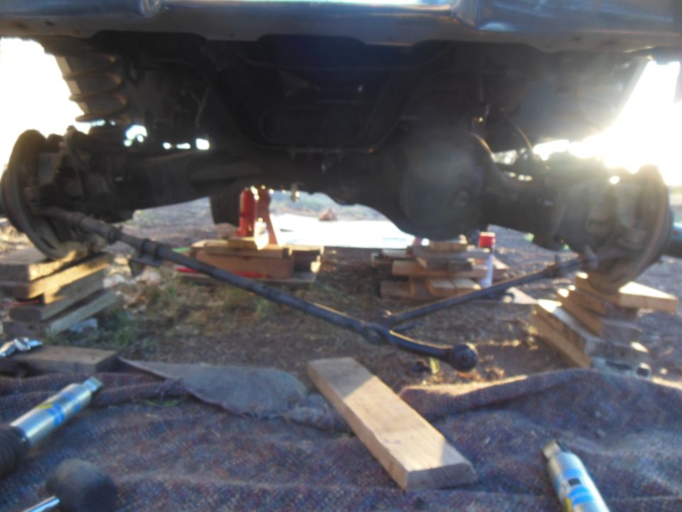 Underside of a Ford Bronco with rear axle supported by blocks, steering linkage and shock visible.