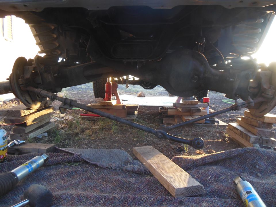 Undercarriage of a vehicle on blocks and jacks, showing front axle and steering linkage.