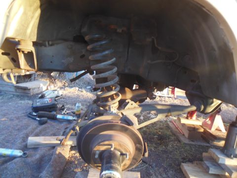1984 Ford Bronco - The underside of a vehicle is shown, with a large coil spring and suspension components visible. Tools and parts, including a shock absorbe…
