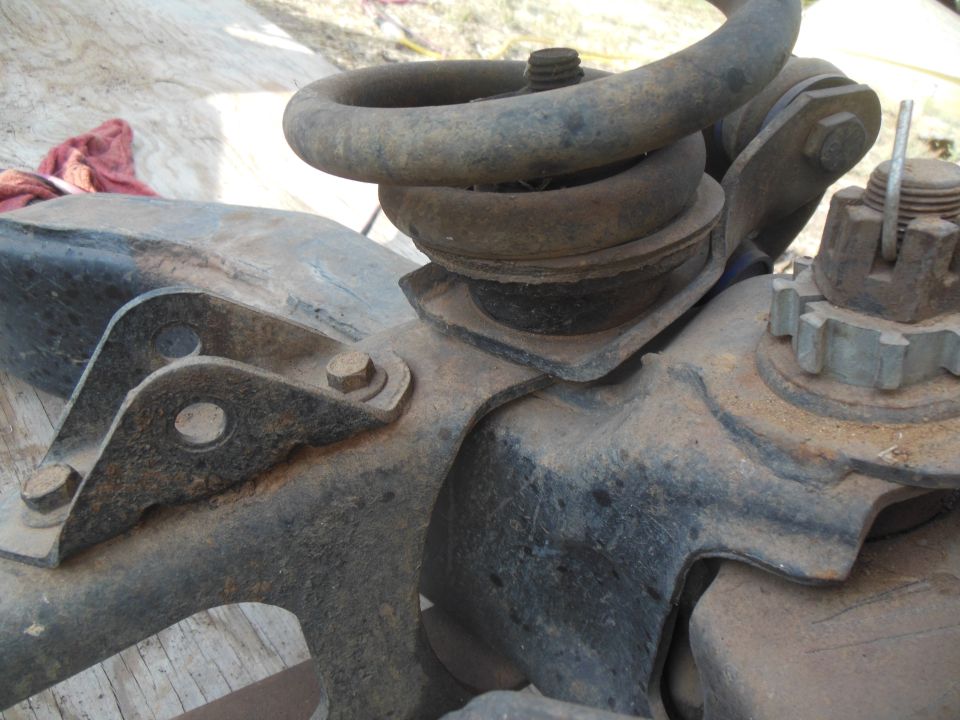 Close-up of rusted vehicle suspension parts: coil spring, brackets, and a castle nut.