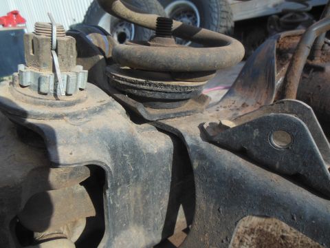 1984 Ford Bronco - A close-up view of rusty, dirty automotive suspension components, including a coil spring and a castle nut with a cotter pin.