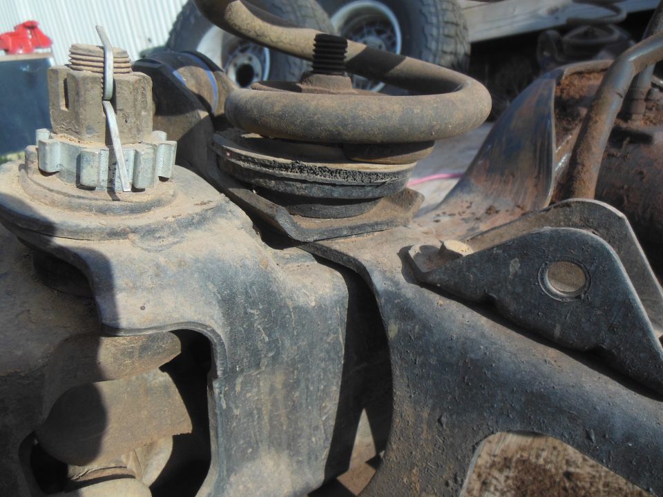 Close-up of rusty automotive suspension parts: coil spring, castle nut, cotter pin.