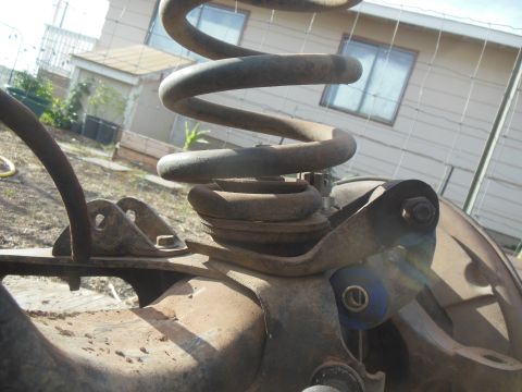 1984 Ford Bronco - A close-up, low-angle shot of rusty suspension components from a 1984 Ford Bronco, including a coil spring and part of the wheel hub, outdo…