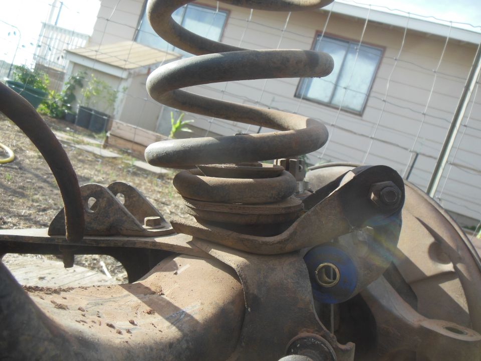 Rusty coil spring and suspension parts of a 1984 Ford Bronco.