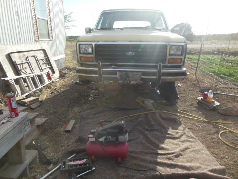 1984 Ford Bronco - A tan 1980s Ford truck or SUV is parked outdoors in front of a mobile home. Tools and an air compressor are laid out on the ground in front…