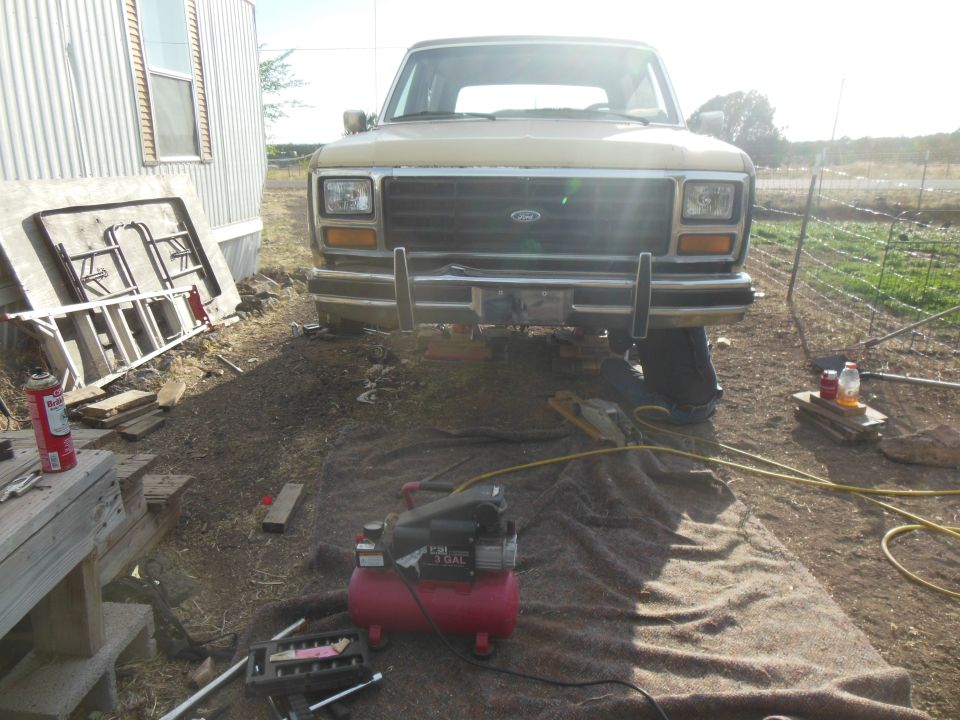 Tan 1980s Ford truck or SUV parked outdoors with tools and air compressor.