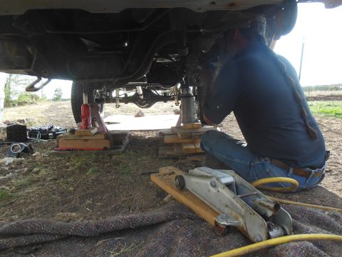 1984 Ford Bronco - A person is working underneath a lifted vehicle, likely a 1984 Ford Bronco, with the frame supported by red and silver hydraulic jacks and…