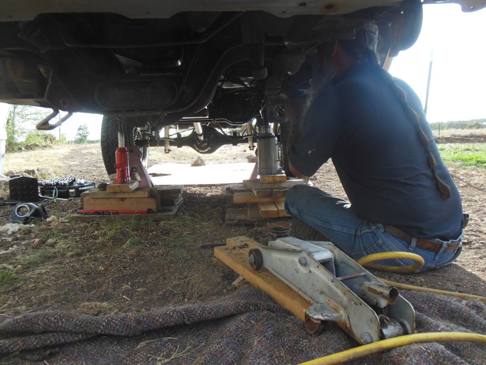 Underneath a lifted 1984 Ford Bronco, supported by jacks, with a person working on it.