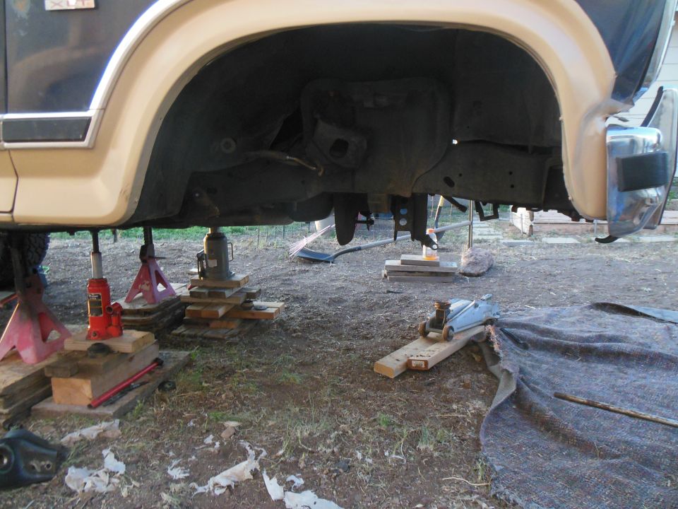 Vehicle underside supported by jack stands and blocks, with a floor jack on a ramp.
