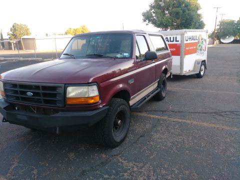 1996 Ford Bronco - A maroon 1996 Ford Bronco is parked next to a white U-Haul trailer. The Bronco has a custom black bumper and side steps.