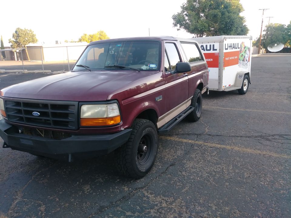 Maroon 1996 Ford Bronco with custom bumper and side steps towing a U-Haul trailer.