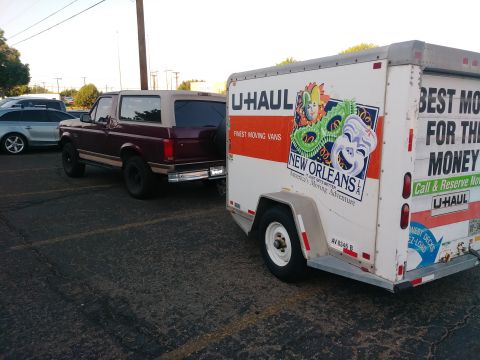 1996 Ford Bronco - A maroon Ford Bronco with a tan top is parked next to a U-Haul trailer. The Bronco is viewed from the rear passenger side, and the trailer…