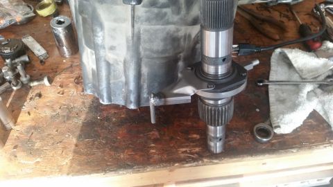 1985 Ford Bronco - A close-up view of a transmission or transfer case part with a splined shaft and gears, resting on a wooden workbench. Various tools and ha…