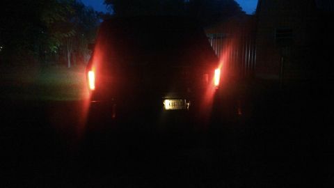 1978 Ford Bronco - The rear of a dark-colored SUV is visible at night, with its red taillights illuminated. A license plate reading "K867LS" is mounted on the…