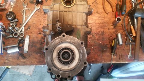 1985 Ford Bronco - A disassembled transmission or transfer case sits on a wooden workbench surrounded by tools and hardware. The main component is a large, re…