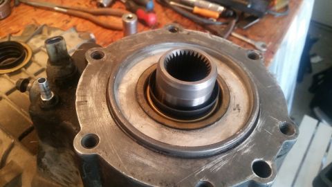1985 Ford Bronco - A close-up view of a heavily used transfer case with a splined input shaft and a metal housing. Several tools and parts are visible in the…