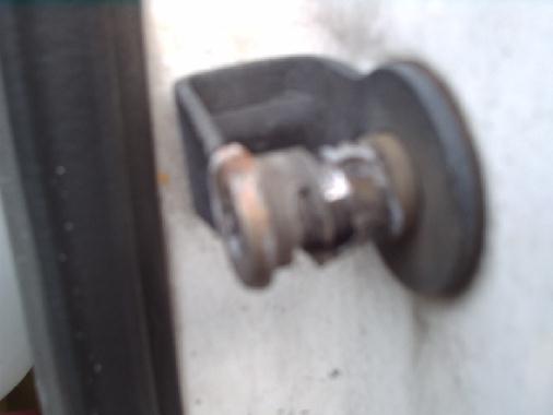 Blurry close-up of a rusty door hinge or latch component near a body panel edge