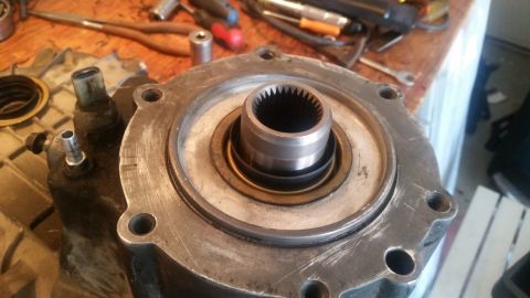 1985 Ford Bronco - A close-up view of a transfer case housing with a splined input shaft protruding from the center. Several tools and other vehicle parts are…