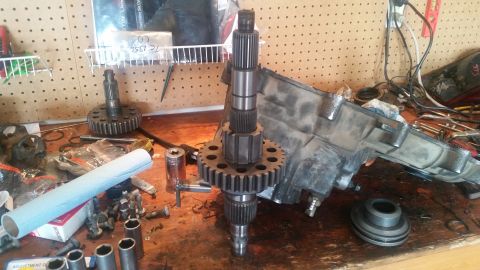 1985 Ford Bronco - A workbench displays disassembled transmission parts, including gears and shafts, alongside tools and a roll of blue shop towels. A metal t…