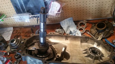 1985 Ford Bronco - A disassembled transfer case is laid out on a wooden workbench. A main shaft with splines sits vertically in the center of the transfer cas…