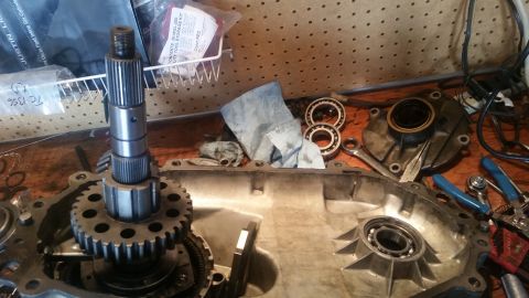 1985 Ford Bronco - A disassembled transfer case is laid out on a wooden workbench. A large gear is attached to a shaft, and several bearings and tools are sca…
