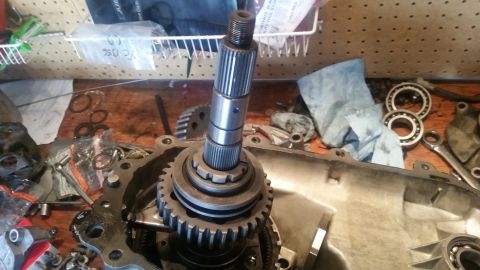 1985 Ford Bronco - A close-up view of a transfer case assembly with a splined input shaft and gears. Various tools and bearings are scattered around the workb…