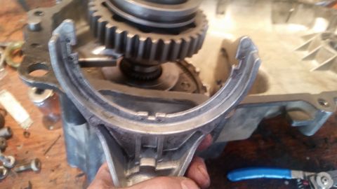 1985 Ford Bronco - A close-up view shows a metal fork-like part being held in front of a partially disassembled transmission or transfer case. Gears are visib…