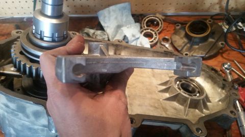 1985 Ford Bronco - A person's hand holds a metal component over a disassembled mechanical assembly, likely part of a vehicle's drivetrain. Gears, bearings, an…
