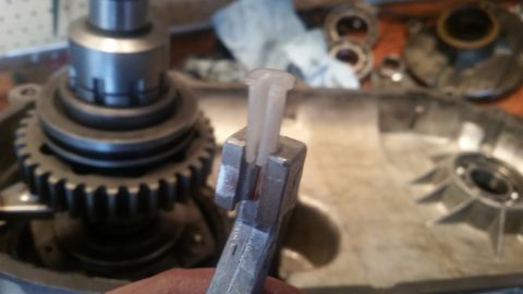 1985 Ford Bronco - A close-up shot shows a metal tool holding a white plastic component, with a gear and part of a transmission visible in the background.