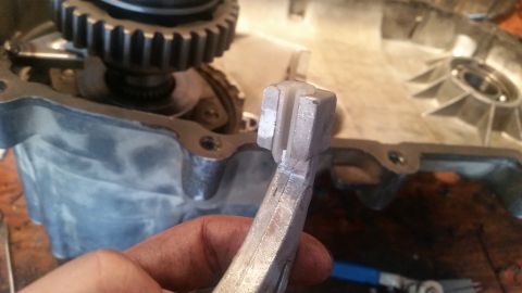 1985 Ford Bronco - A close-up shot shows a hand holding a metal tool with a U-shaped end, positioned over a disassembled vehicle transmission or gearbox. The…