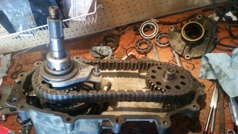 1985 Ford Bronco - A transfer case is disassembled on a wooden workbench, with various gears, bearings, and a chain visible. The internal components of the tr…