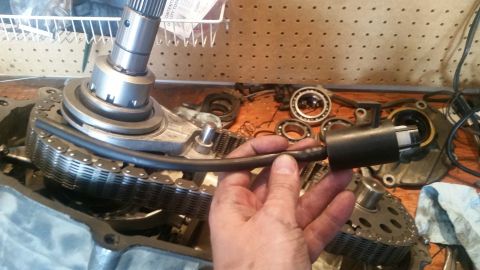 1985 Ford Bronco - A person holds a metal tube connected to a black cylindrical component over a disassembled transfer case with a chain drive. Various gears…