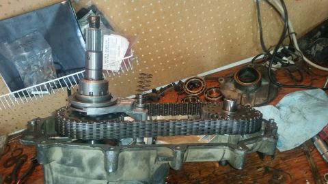 1985 Ford Bronco - A disassembled transfer case is laid out on a wooden surface. The internal components, including gears and a chain, are visible, along with…