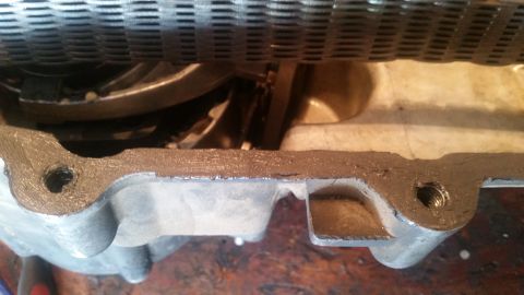 1985 Ford Bronco - A close-up view shows a metal engine part with a gasket and threaded bolt holes, likely from a 1985 Ford Bronco. The part is covered in a d…