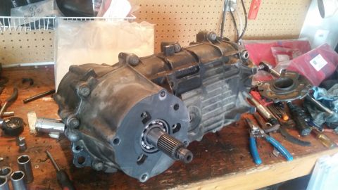 1985 Ford Bronco - A transfer case assembly, likely from a 1985 Ford Bronco, is laid out on a workbench with various tools. A bearing is visible on the input…