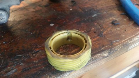1985 Ford Bronco - A yellow plastic part with ribbed sides and a hexagonal outer edge sits on a weathered wooden surface. The part appears to be a bearing or…