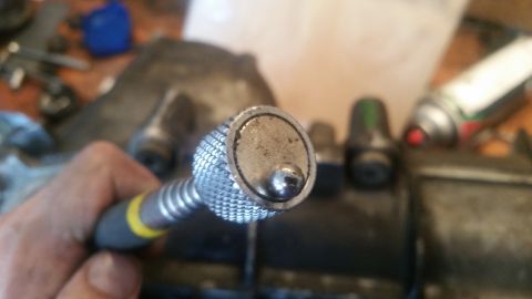 1985 Ford Bronco - A close-up shot shows a hand holding a knurled metal tool with a small ball bearing on the end. The background is blurred and shows various…