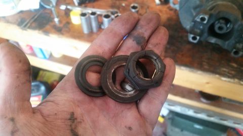 1985 Ford Bronco - A hand holds three metal parts on a workbench. The parts appear to be a nut and two washers, possibly from a vehicle's suspension or drivet…
