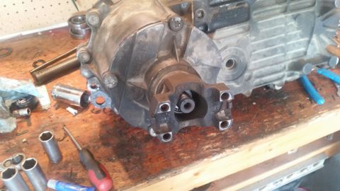 1985 Ford Bronco - A close-up view of a transfer case or transmission output shaft with a yoke attached, resting on a wooden workbench. Various tools, includi…