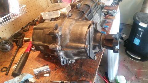 1985 Ford Bronco - A transfer case sits on a workbench alongside various tools, including a hammer, socket wrench, and bearing.