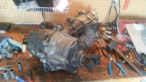 1985 Ford Bronco - A transfer case sits on a workbench surrounded by various tools, including sockets, pliers, and a hammer. The transfer case is made of meta…