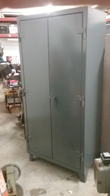 1995 Ford Bronco - A tall, gray metal cabinet with double doors stands in a workshop setting. The cabinet has silver handles and hinges, and it is raised on s…