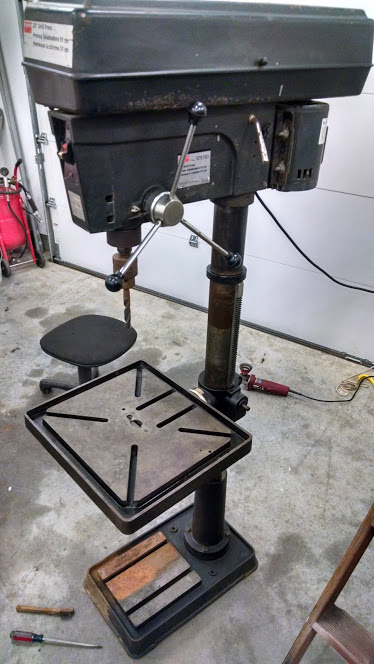1995 Ford Bronco - A black drill press is shown in a garage setting with a stool and tools nearby.