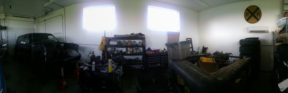Dark SUV with hood open in a cluttered garage with tools and tires.
