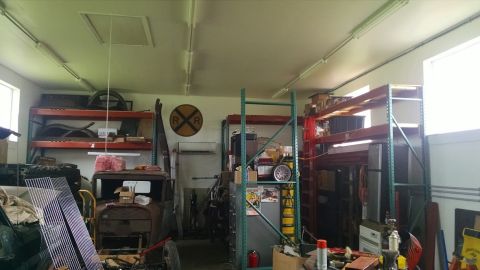 1995 Ford Bronco - A rusty, vintage car body sits in a cluttered garage with shelves full of parts and equipment. The car appears to be an early model, possib…
